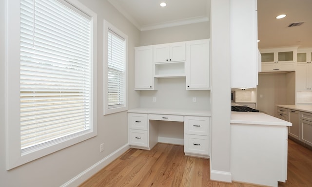 unfurnished office featuring light hardwood / wood-style floors, ornamental molding, and built in desk