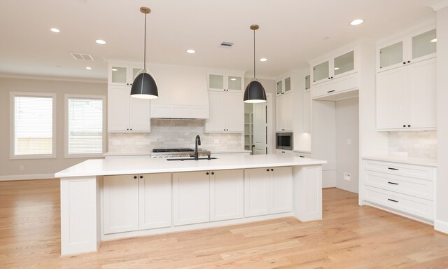 kitchen featuring ornamental molding, a kitchen island with sink, decorative light fixtures, and backsplash