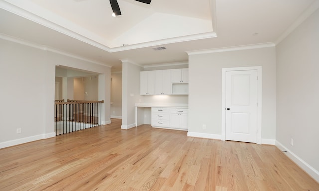 unfurnished living room featuring built in desk, ceiling fan, a tray ceiling, light hardwood / wood-style flooring, and crown molding