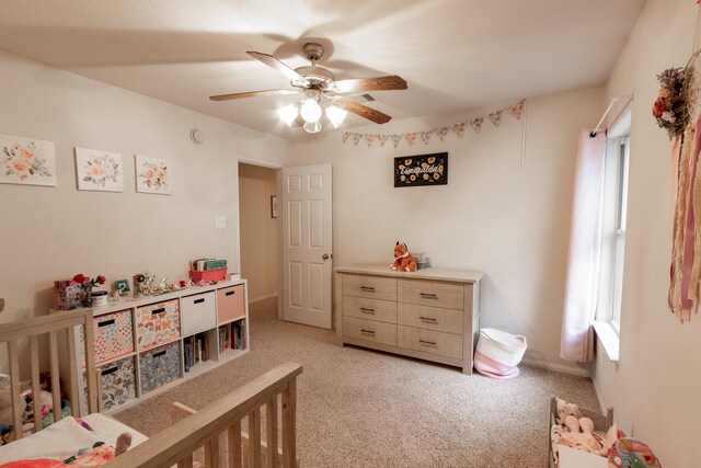 carpeted bedroom featuring a nursery area and ceiling fan