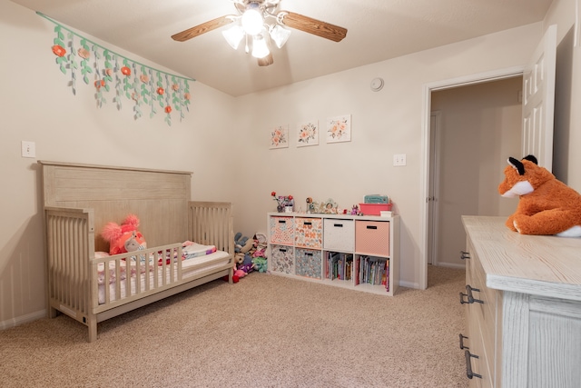 carpeted bedroom with a crib and ceiling fan