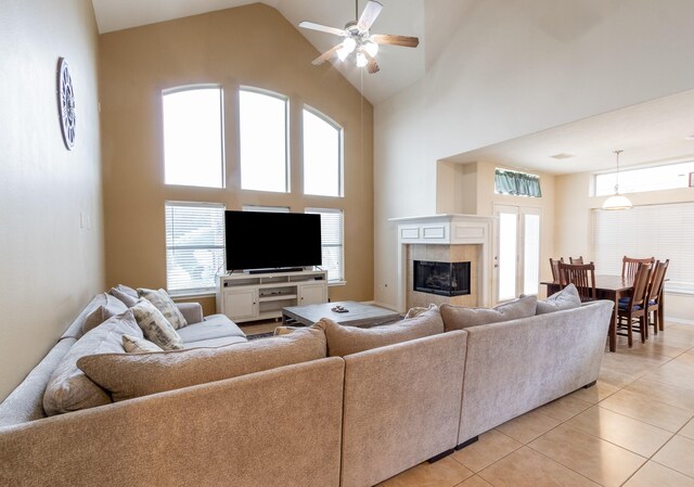 living room with light tile patterned flooring, a tile fireplace, ceiling fan, and high vaulted ceiling