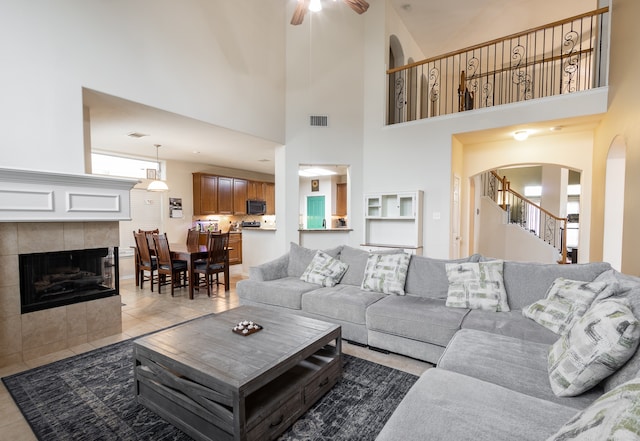 tiled living room featuring a fireplace, ceiling fan, and a towering ceiling