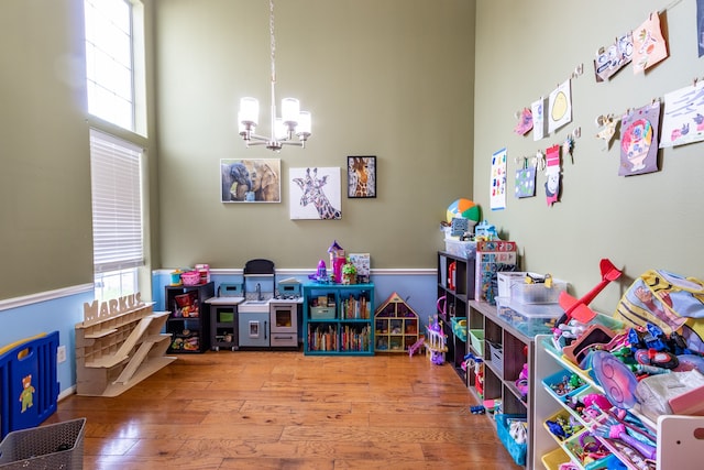 rec room with a notable chandelier, hardwood / wood-style floors, and a towering ceiling