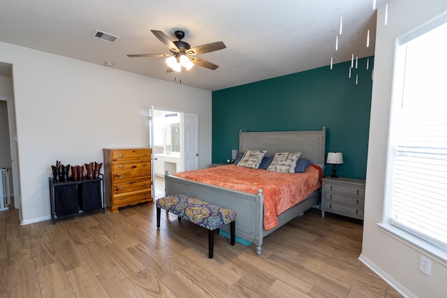 bedroom featuring ceiling fan, multiple windows, ensuite bathroom, and hardwood / wood-style flooring