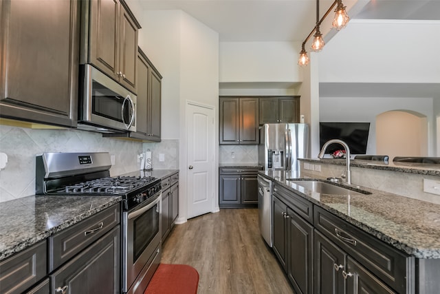 kitchen featuring appliances with stainless steel finishes, dark brown cabinetry, sink, wood-type flooring, and stone countertops