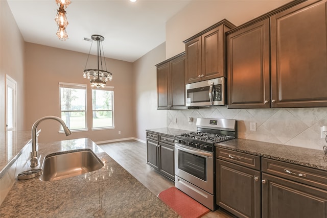 kitchen with appliances with stainless steel finishes, light wood-type flooring, tasteful backsplash, sink, and a chandelier