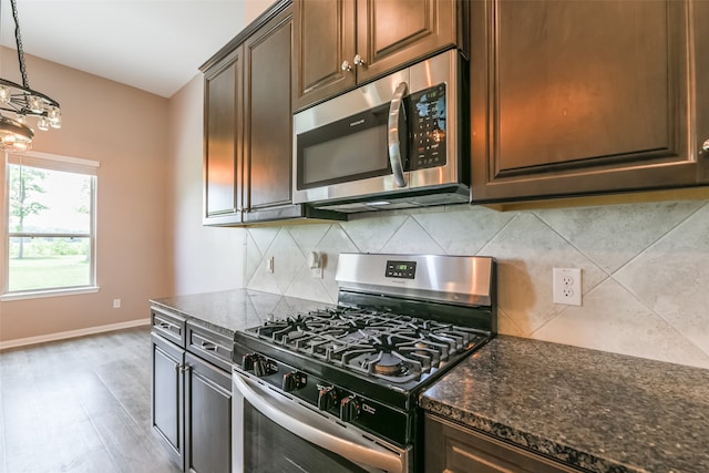 kitchen with stainless steel appliances, backsplash, dark stone countertops, wood-type flooring, and dark brown cabinets