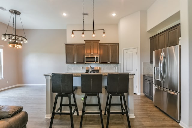 kitchen with appliances with stainless steel finishes, a kitchen breakfast bar, a center island with sink, light hardwood / wood-style flooring, and hanging light fixtures