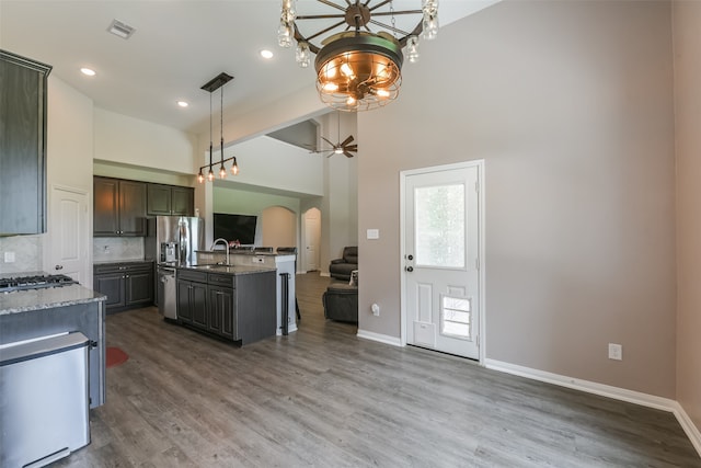 kitchen featuring dark hardwood / wood-style flooring, light stone counters, ceiling fan with notable chandelier, sink, and an island with sink