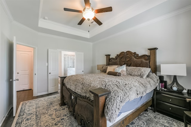 bedroom featuring ensuite bath, a raised ceiling, ceiling fan, crown molding, and hardwood / wood-style flooring