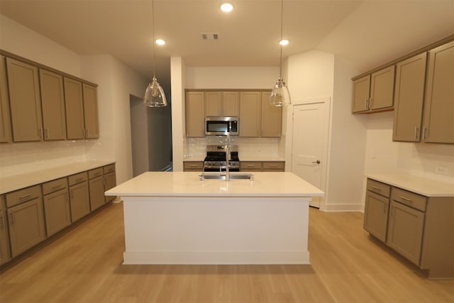 kitchen featuring sink, light hardwood / wood-style flooring, appliances with stainless steel finishes, an island with sink, and decorative light fixtures