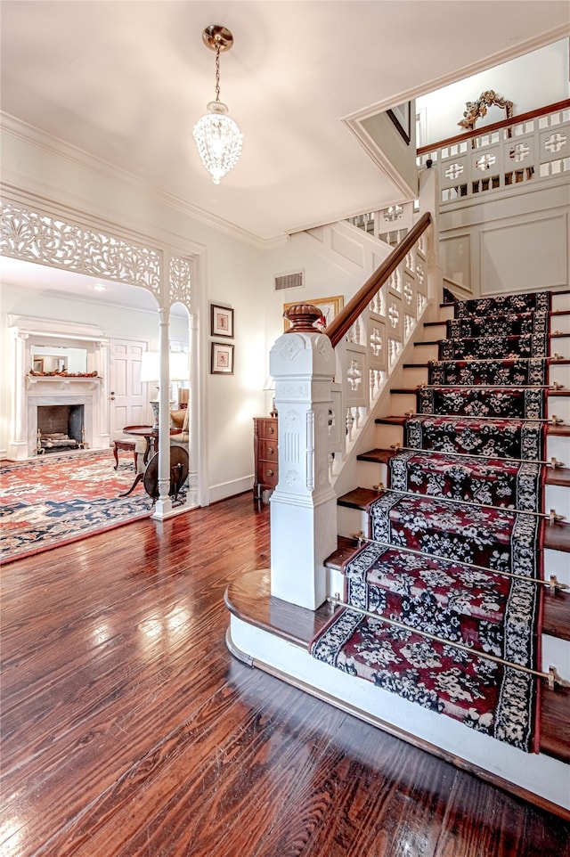 stairs with a chandelier, dark hardwood / wood-style flooring, crown molding, ornate columns, and a high end fireplace