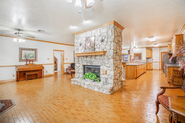 living room with a textured ceiling, a fireplace, ornamental molding, light wood-type flooring, and ceiling fan