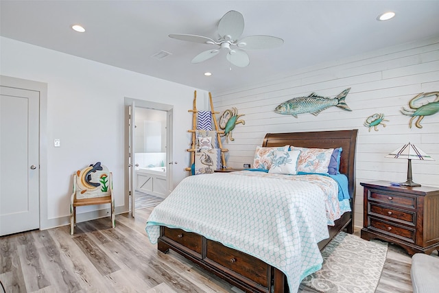 bedroom featuring ensuite bathroom, ceiling fan, light wood-type flooring, and wood walls