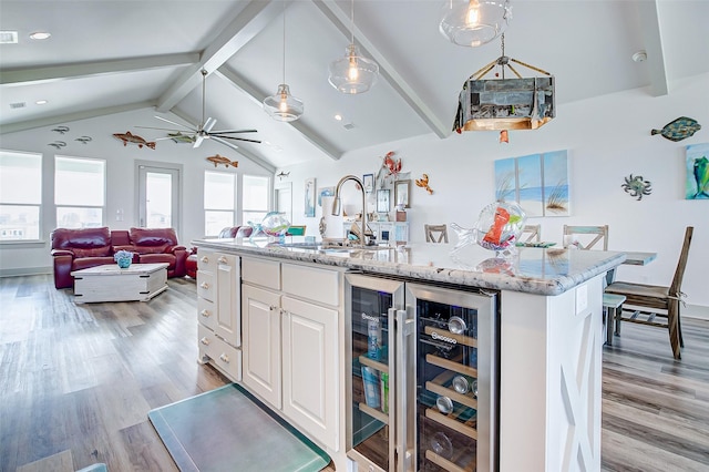 kitchen featuring wine cooler, decorative light fixtures, sink, a kitchen island with sink, and white cabinets