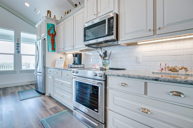 kitchen featuring light stone countertops, lofted ceiling, white cabinetry, stainless steel appliances, and light wood-type flooring