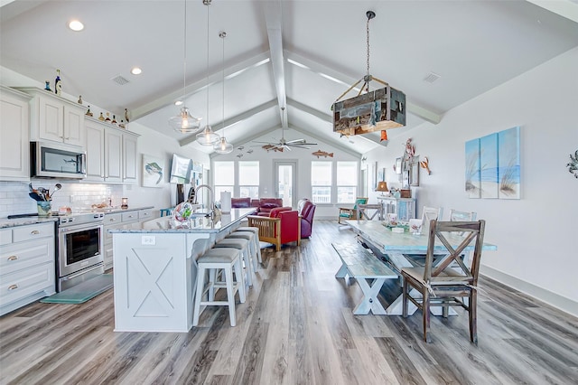 kitchen with ceiling fan, lofted ceiling with beams, a kitchen bar, appliances with stainless steel finishes, and an island with sink