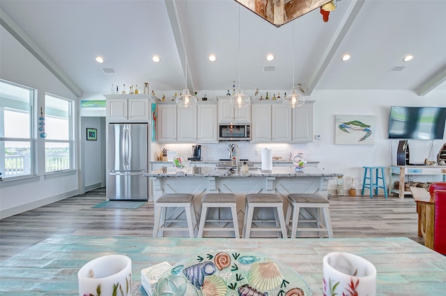 kitchen with a center island with sink, stainless steel appliances, white cabinets, and light stone counters