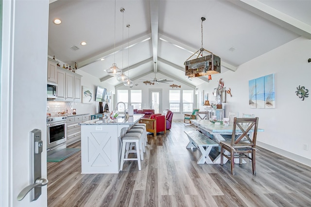 kitchen with ceiling fan, appliances with stainless steel finishes, decorative backsplash, a kitchen island with sink, and pendant lighting