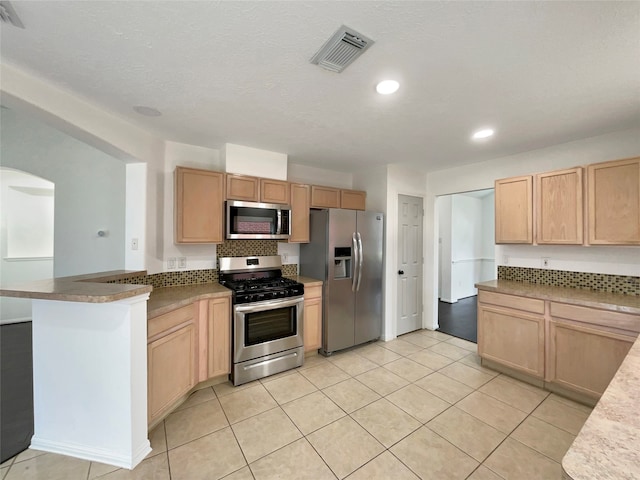 kitchen featuring light brown cabinets, kitchen peninsula, stainless steel appliances, and light tile patterned floors