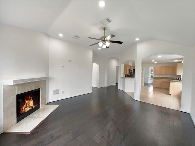 unfurnished living room with ceiling fan, sink, light hardwood / wood-style flooring, a tiled fireplace, and lofted ceiling