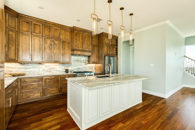 kitchen with light stone countertops, sink, hanging light fixtures, stainless steel fridge, and a center island with sink