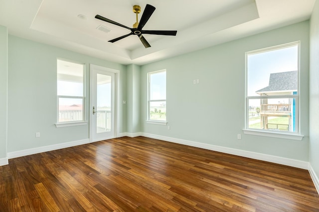 empty room featuring a tray ceiling, dark hardwood / wood-style floors, and a healthy amount of sunlight