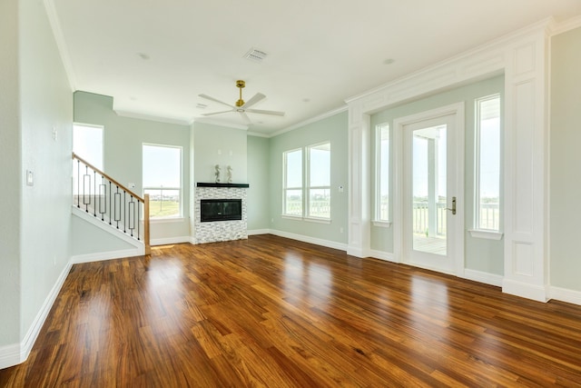 unfurnished living room featuring ceiling fan, dark wood-type flooring, crown molding, and a stone fireplace