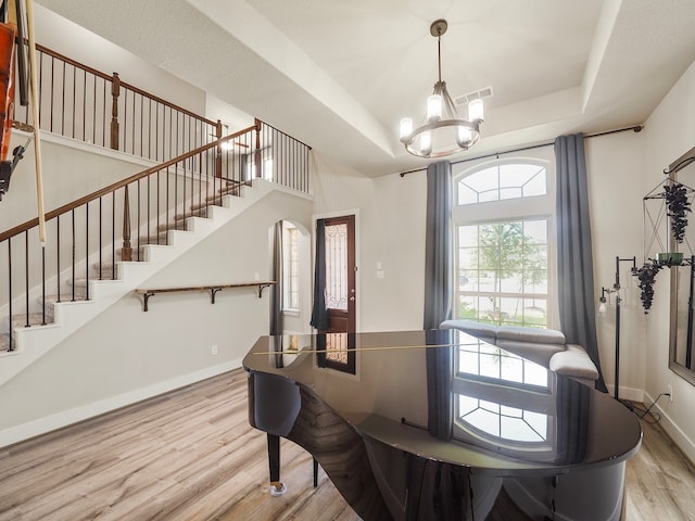 dining space with a raised ceiling, hardwood / wood-style floors, and an inviting chandelier