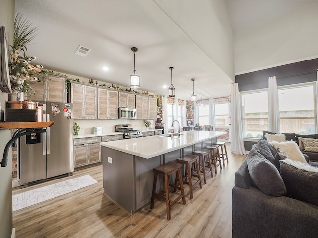 kitchen featuring light wood-type flooring, an island with sink, sink, appliances with stainless steel finishes, and a kitchen bar