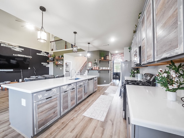 kitchen featuring light wood-type flooring, a center island with sink, stainless steel appliances, pendant lighting, and sink