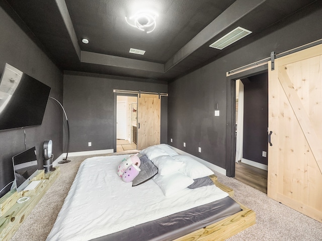 bedroom featuring carpet, a tray ceiling, and a barn door