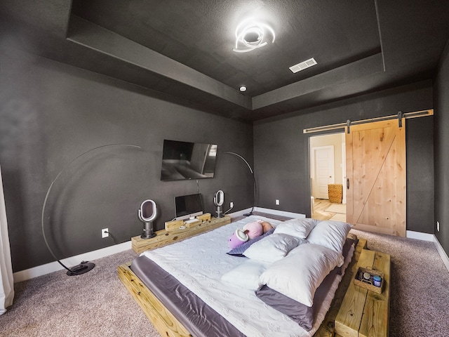 carpeted bedroom featuring a raised ceiling and a barn door