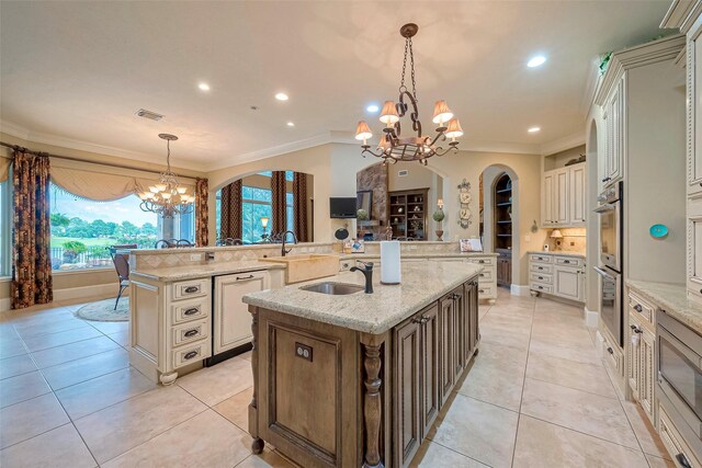 kitchen with a chandelier, hanging light fixtures, an island with sink, sink, and light tile patterned floors