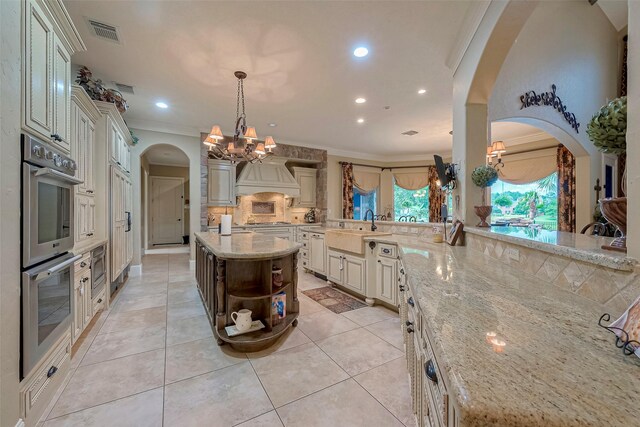 kitchen featuring a notable chandelier, tasteful backsplash, stainless steel appliances, light stone countertops, and custom exhaust hood