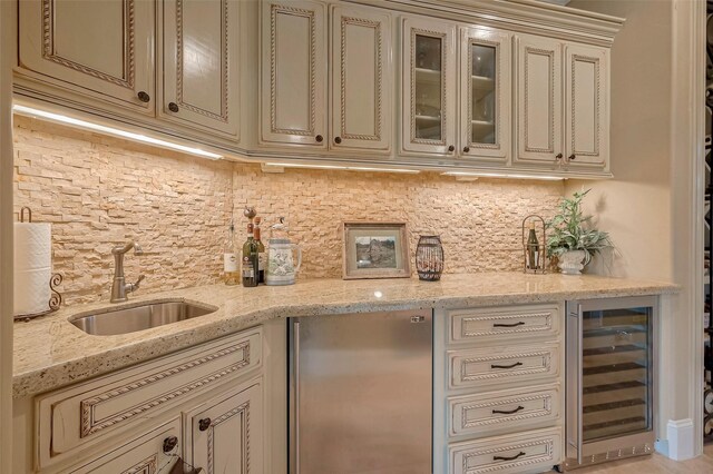 kitchen featuring beverage cooler, cream cabinetry, sink, light stone countertops, and stainless steel refrigerator