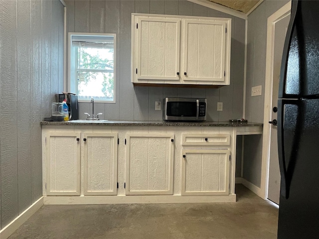 kitchen with white cabinets, concrete floors, sink, black fridge, and vaulted ceiling