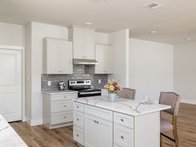 kitchen with electric stove, decorative backsplash, a center island, a kitchen bar, and light hardwood / wood-style flooring