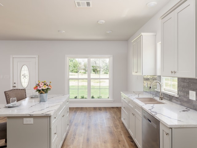 kitchen featuring stainless steel dishwasher, white cabinets, light wood-type flooring, sink, and light stone counters