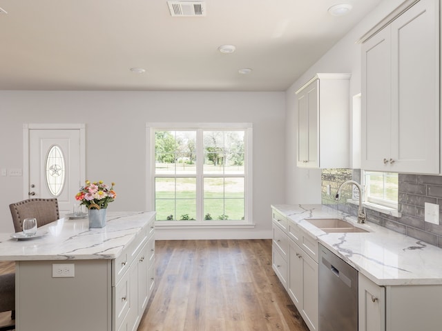 kitchen with sink, light stone counters, white cabinets, a kitchen bar, and stainless steel dishwasher