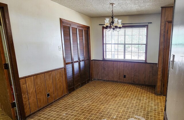 unfurnished dining area featuring a notable chandelier, a textured ceiling, and wooden walls