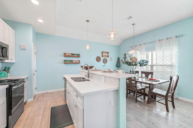 kitchen with appliances with stainless steel finishes, white cabinetry, sink, hanging light fixtures, and a kitchen island with sink