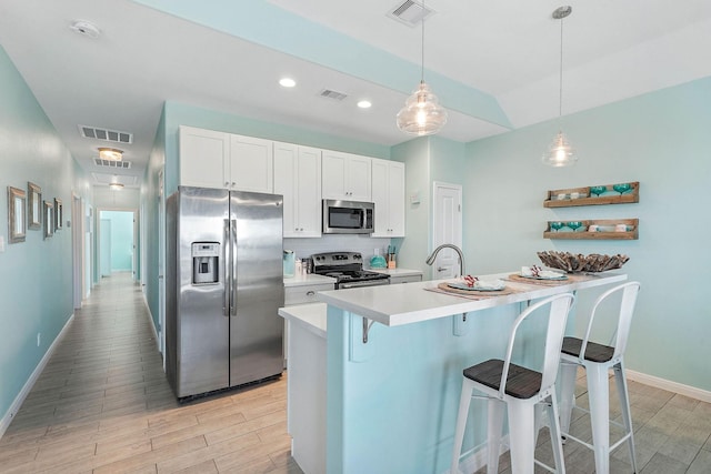 kitchen with a kitchen bar, white cabinetry, decorative light fixtures, appliances with stainless steel finishes, and backsplash