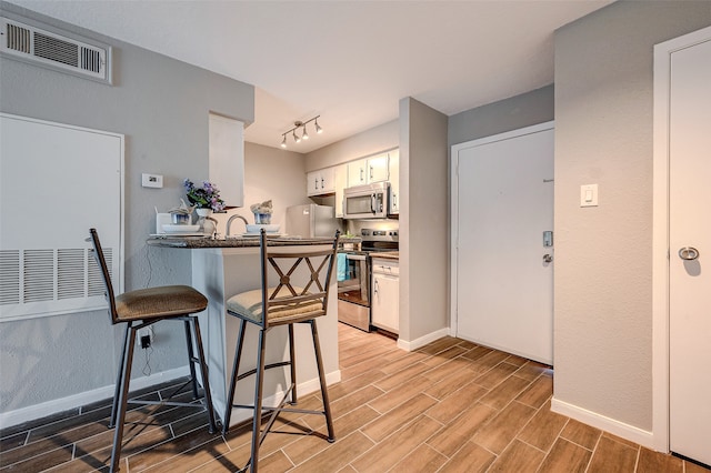 kitchen with light wood-type flooring, a breakfast bar, kitchen peninsula, white cabinetry, and appliances with stainless steel finishes