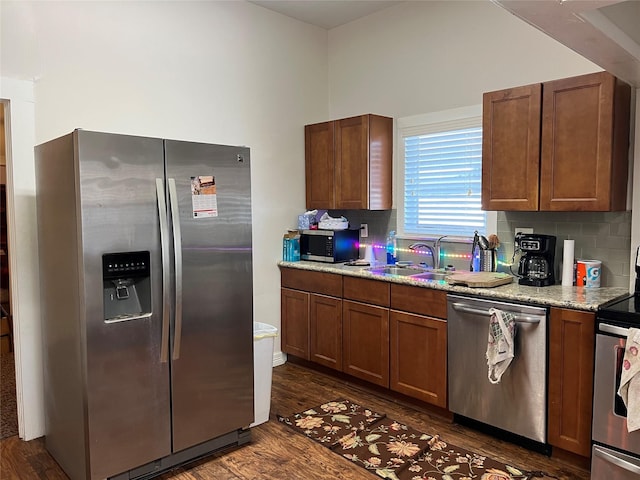 kitchen featuring light stone countertops, sink, dark wood-type flooring, backsplash, and appliances with stainless steel finishes