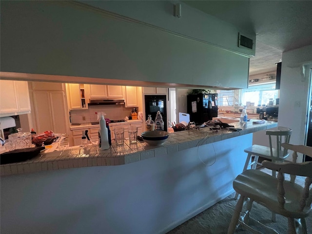 kitchen with dark carpet, a kitchen breakfast bar, black appliances, kitchen peninsula, and white cabinetry