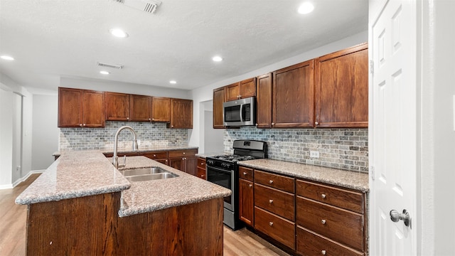 kitchen with sink, light hardwood / wood-style floors, gas stove, a center island with sink, and decorative backsplash