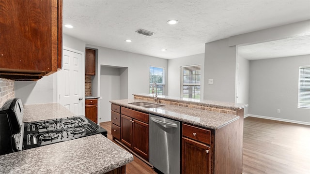 kitchen with sink, hardwood / wood-style flooring, stainless steel dishwasher, a center island with sink, and a textured ceiling