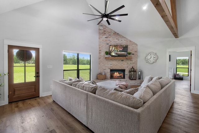 living room with wood-type flooring, ceiling fan, high vaulted ceiling, a brick fireplace, and beam ceiling